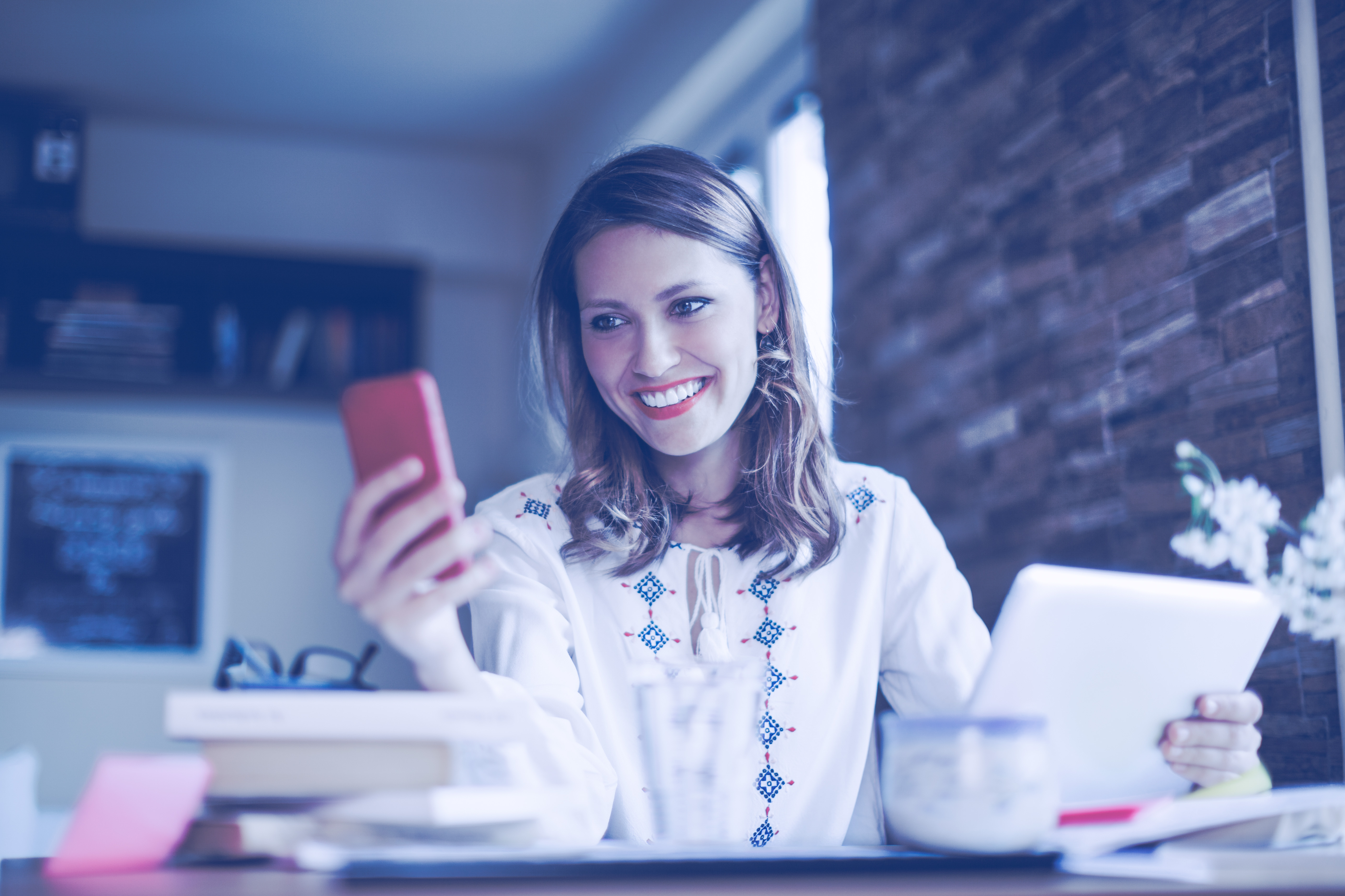 Accounts Payable Automation - Pretty woman is working at home - checking her mobile in one hand and holding her digital tablet in her other hand